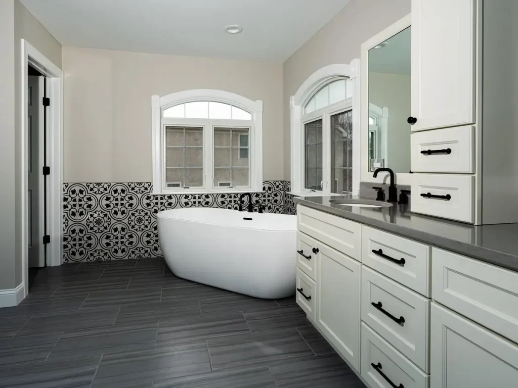 A beautiful bathroom with a freestanding tub, large ceramic tile, and a large vanity with black hardware