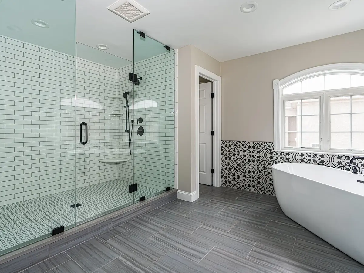 A large tile flooring in a bath with a large tub and spacious glass shower with dark fixtures