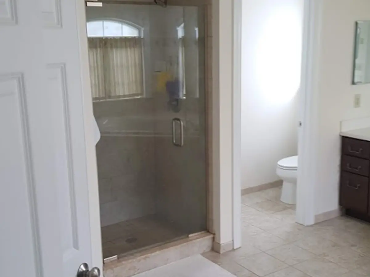 An old bathroom with a glass shower with a curb