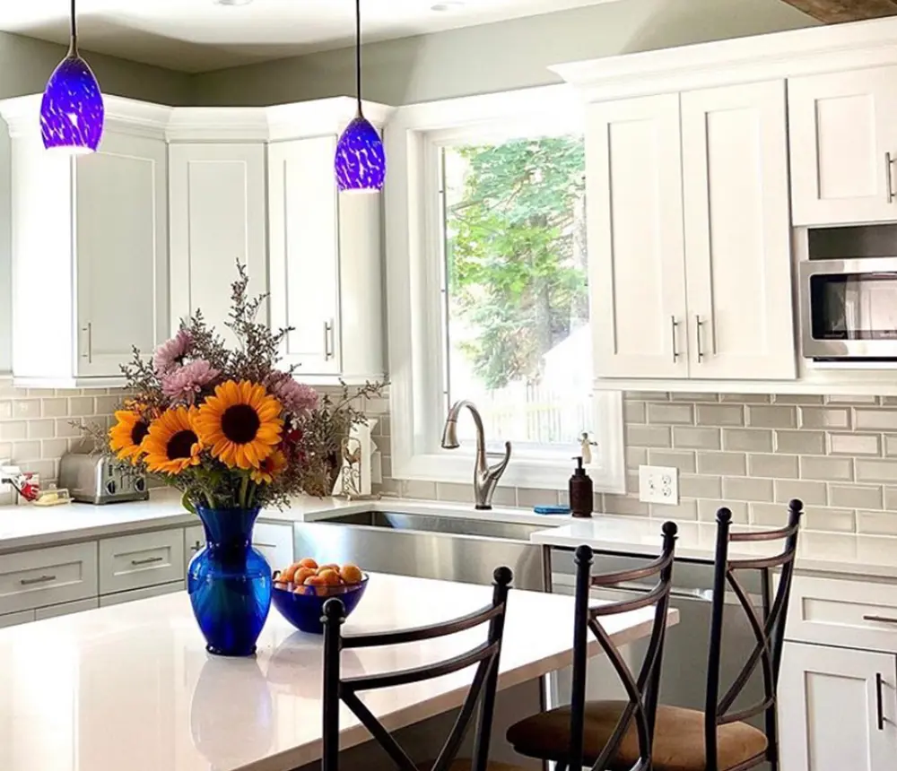 A kitchen with a blue vase on the island and blue pendant lights