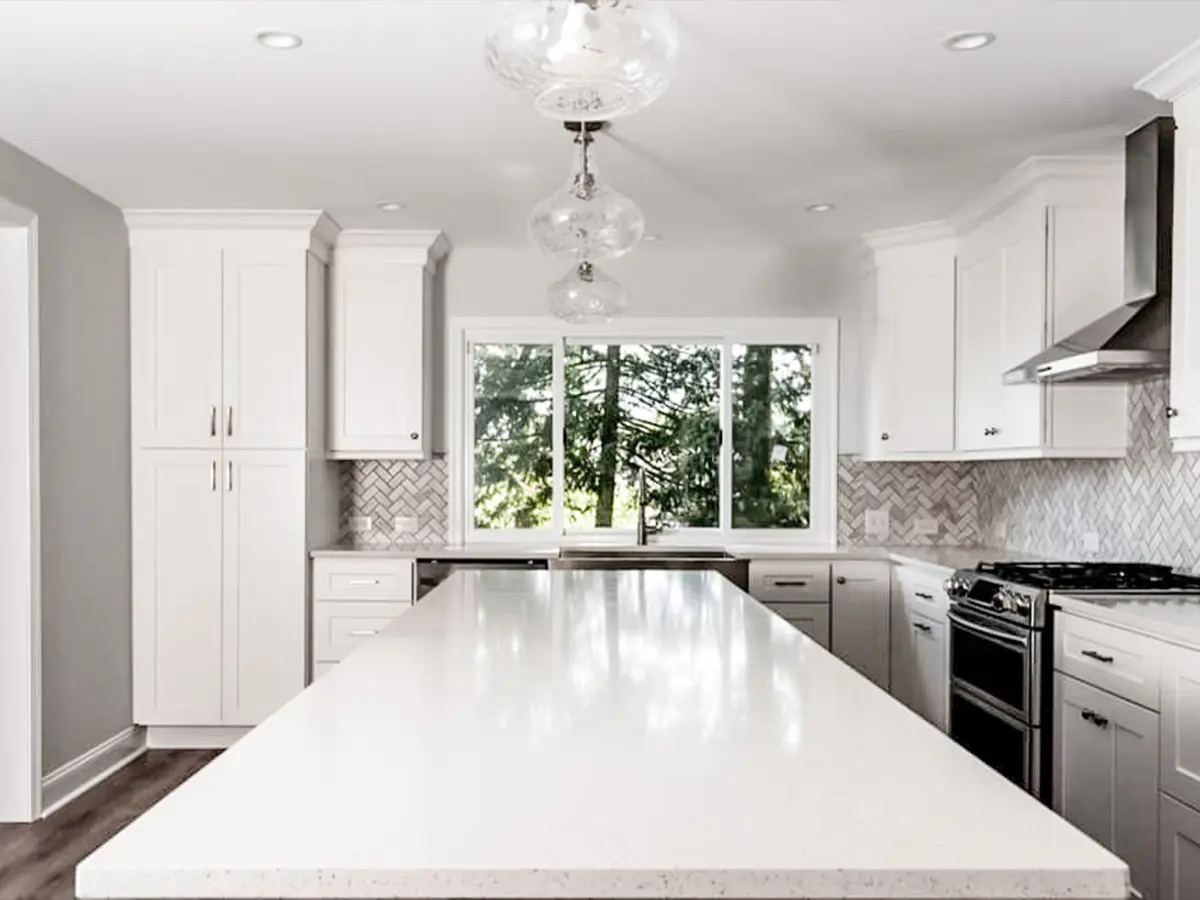 A large kitchen island with white cabinets and herringbone backsplash with tile