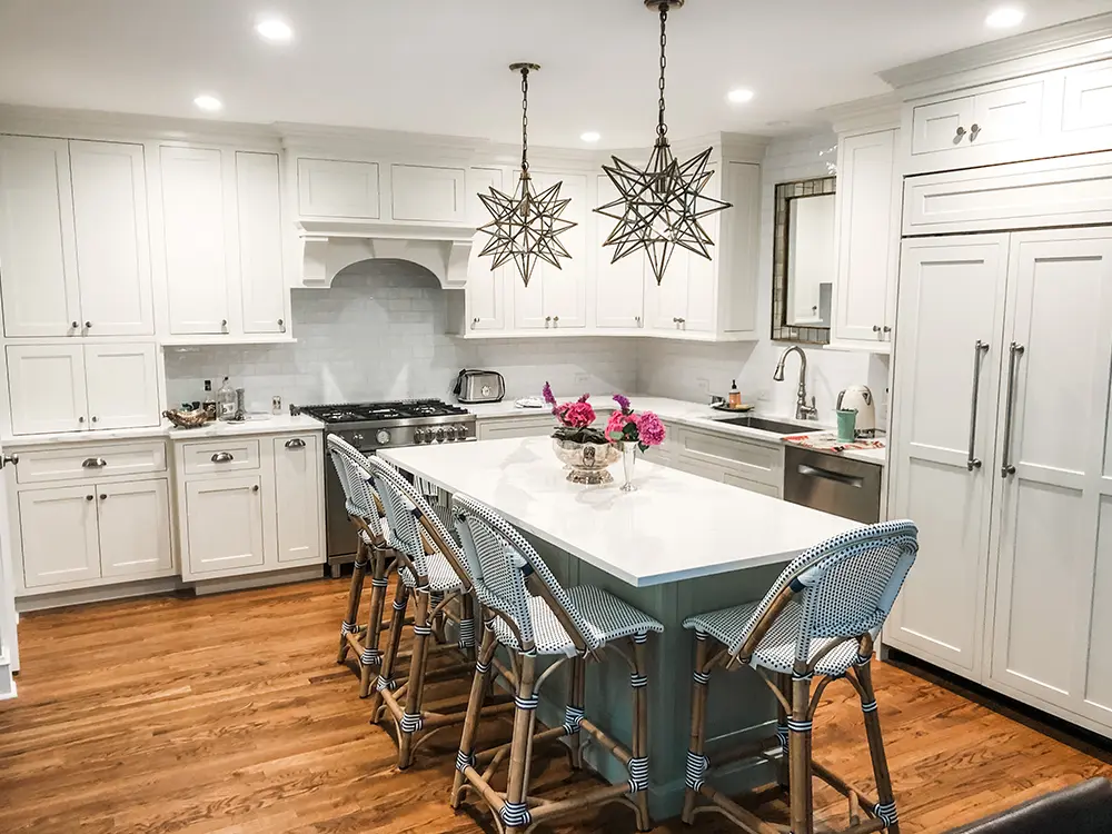 A large kitchen with white cabinets with silver hardware, and quartz countertop