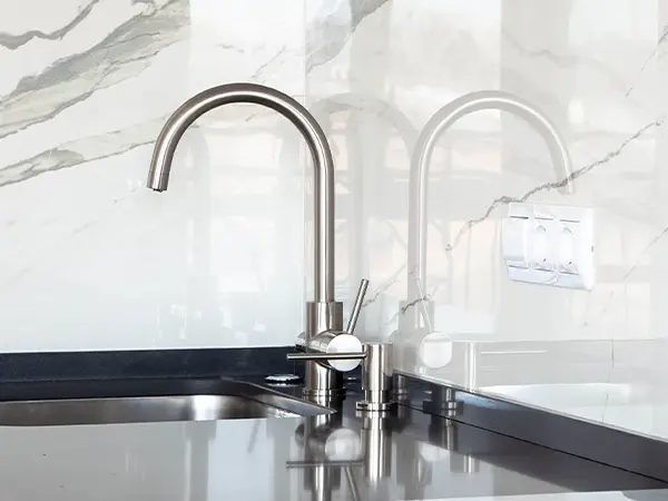 Silver faucet on a dark counter and marble backsplash