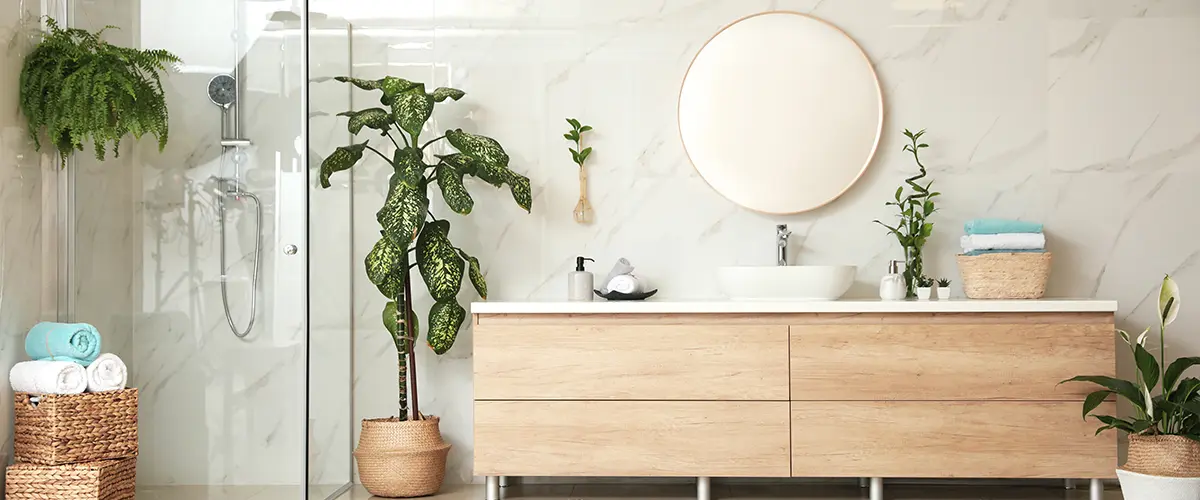A wood vanity with no pulls or knobs in a bath with plants