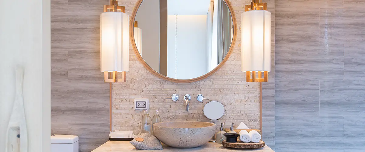 Sconce lights in a bath with round mirror and gold accents