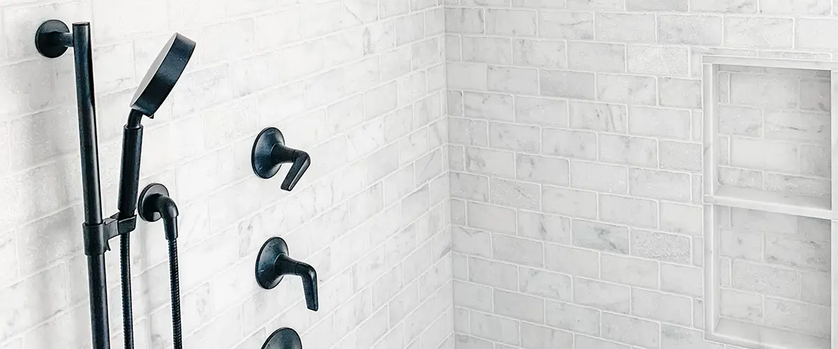 A tiled shower with black water fixtures
