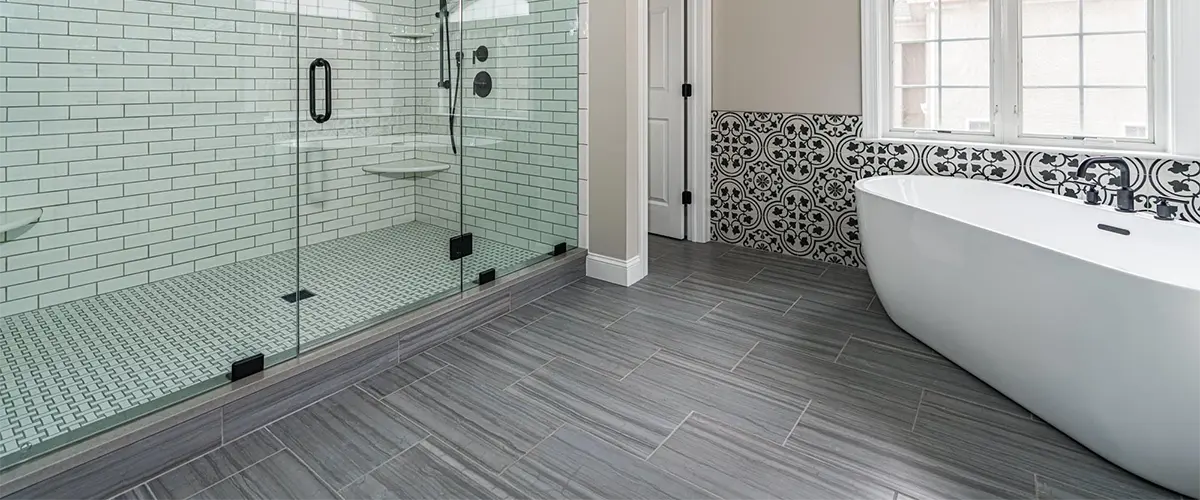 A dark gray tile flooring in a bathroom with a large glass walk-in shower