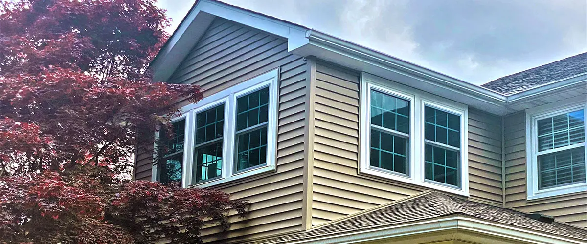 Suburban home with beige siding, white trim, bay windows, under blue sky. Roof Installation Services In Springfield