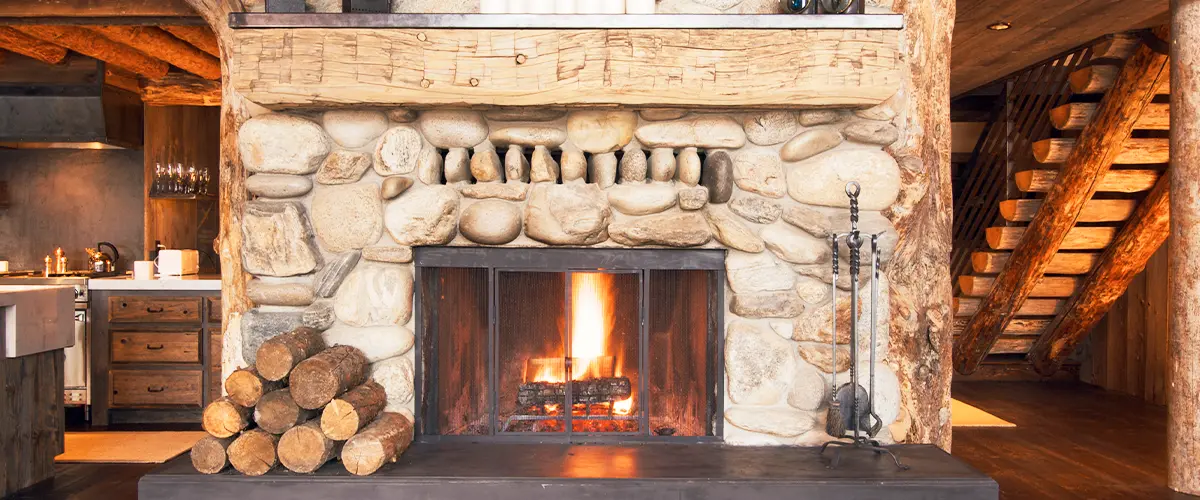 Rustic stone fireplace with a wooden mantel and burning fire in a cozy cabin interior