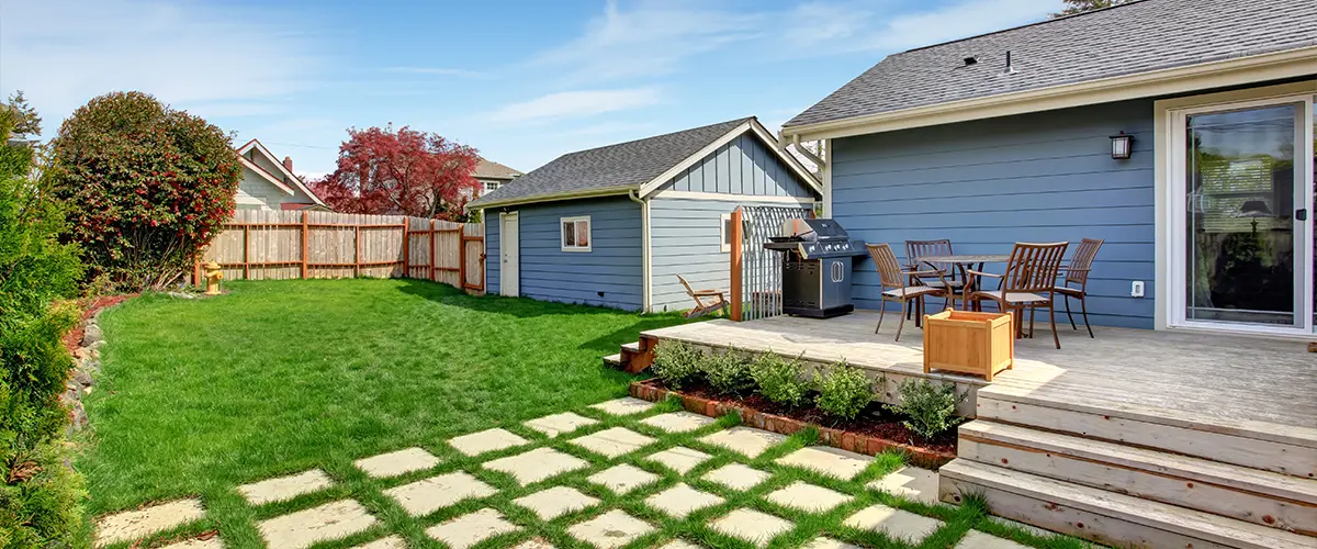 A home addition with green lawn, wood deck, outdoor dining area, and garden landscaping, perfect for relaxation.