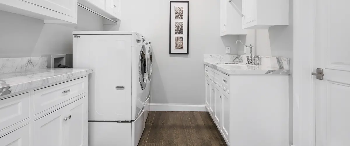 Clean and bright laundry room with white cabinetry, marble countertops, washer, and dryer, providing ample storage space.