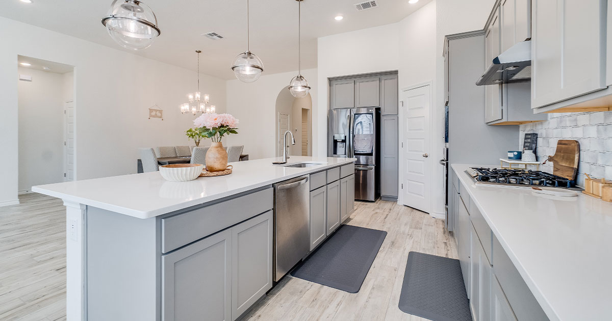 Modern kitchen with gray cabinets, white countertops, stainless steel appliances, pendant lighting, and open dining area.