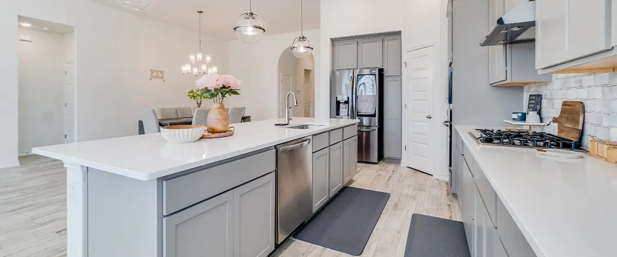 Modern kitchen with gray cabinets, white countertops, stainless steel appliances, pendant lighting, and open dining area.