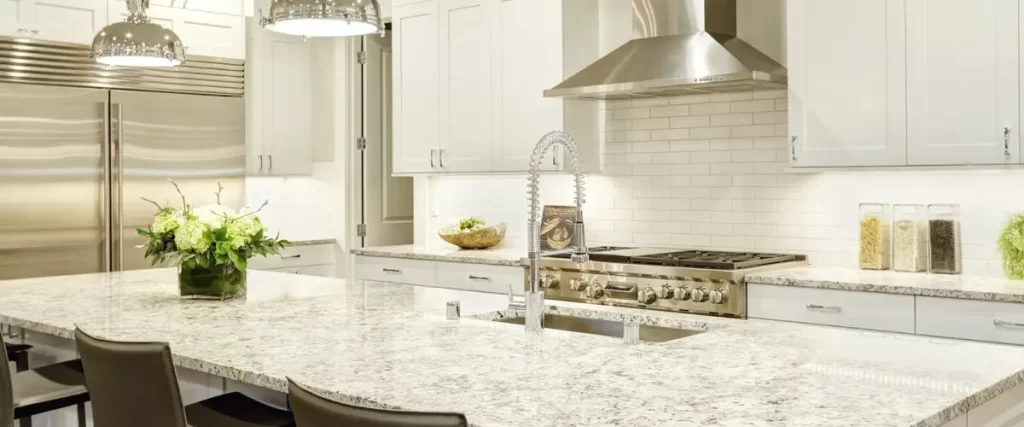 Bright white kitchen with a large granite island, stainless steel appliances, and pendant lighting