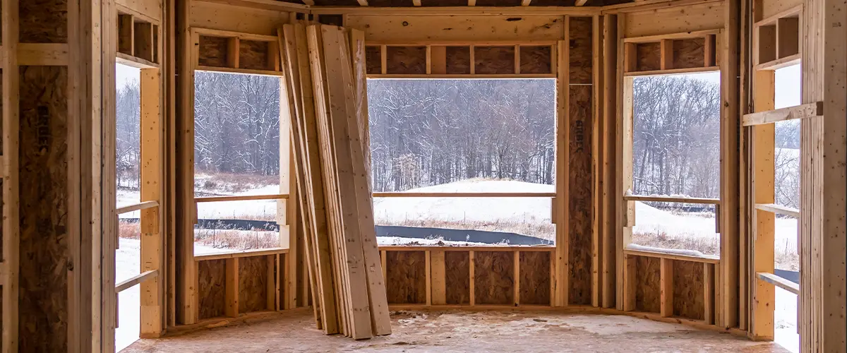 Interior view of a wooden house under construction, overlooking a snowy outdoor landscape.