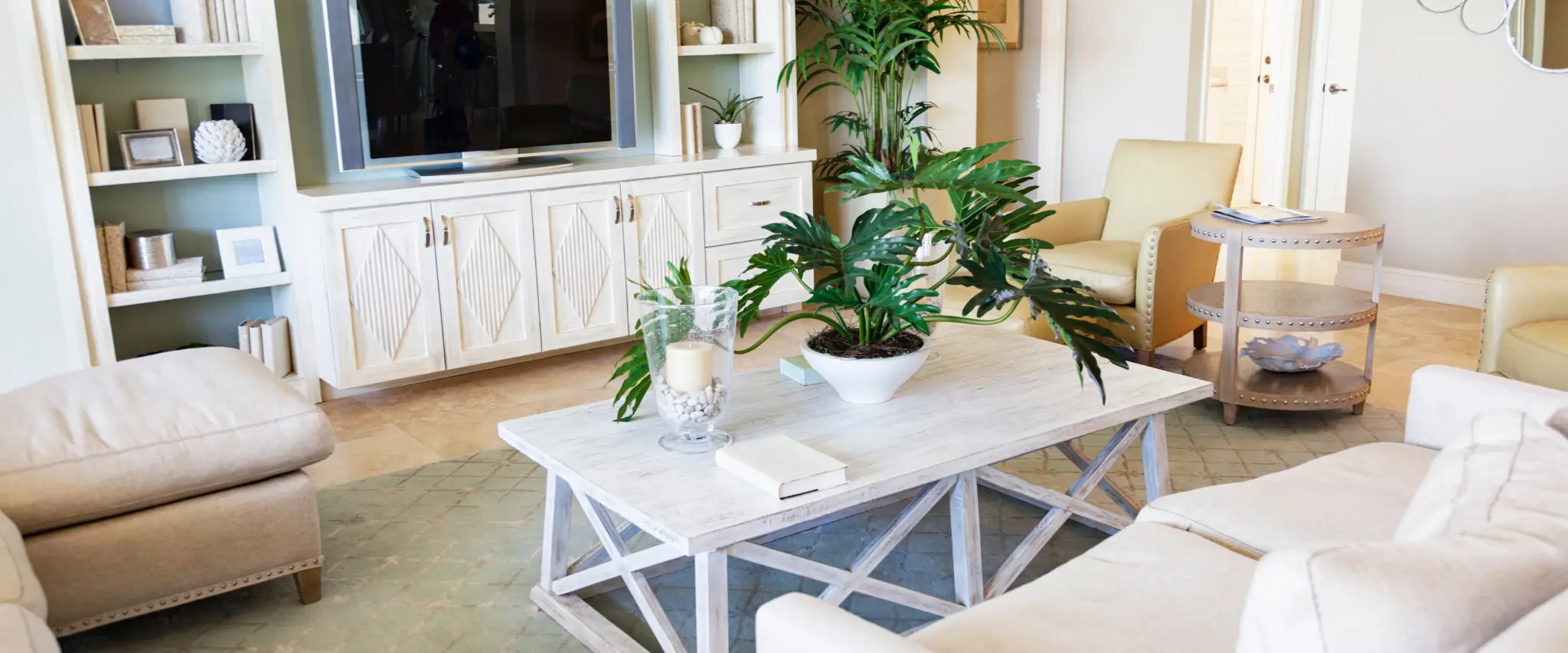 A cozy, coastal-inspired living room with light beige sofas, a white wooden coffee table, and built-in shelves. Green plants and natural textures create a relaxing, beachside ambiance.