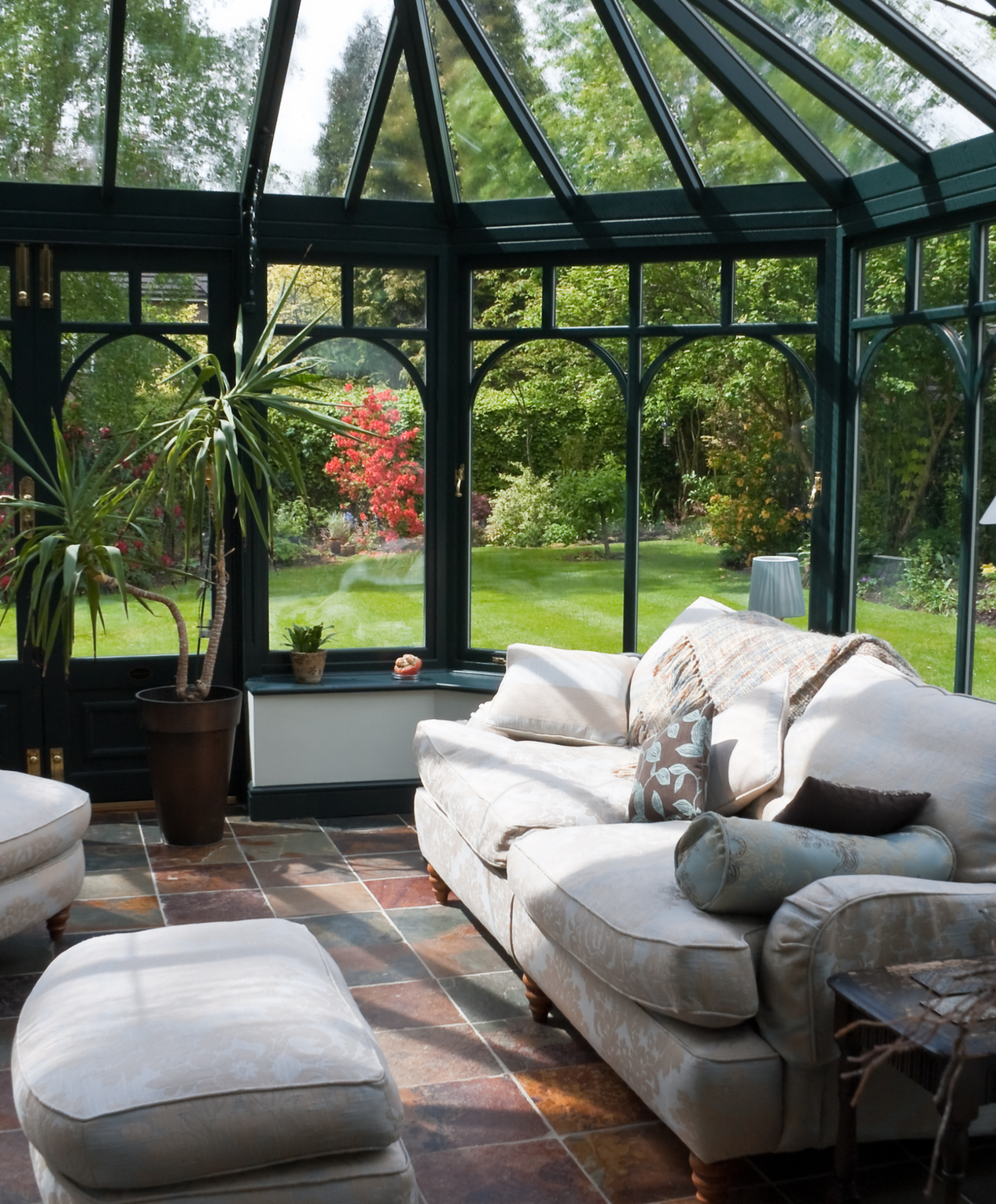 Luxury sunroom with a glass roof and garden views, furnished with elegant seating.