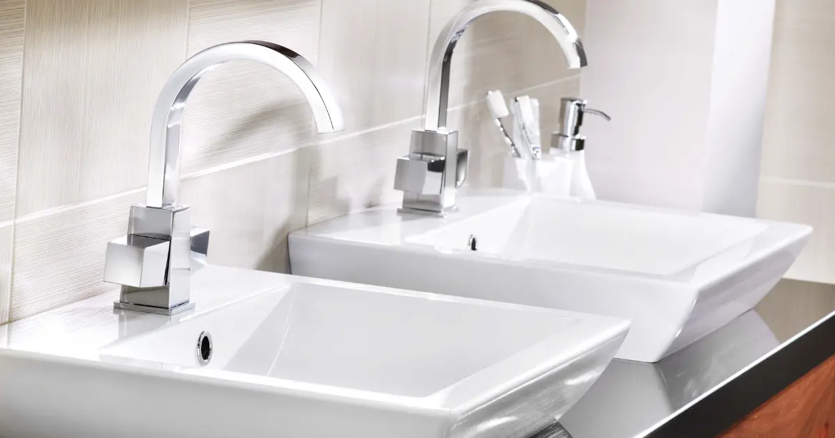 A pair of white sinks with chrome faucets, both running water.