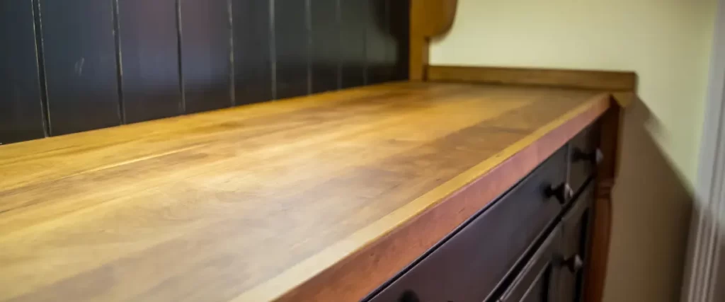 A close-up of a wooden butcher block countertop with a dark backsplash.