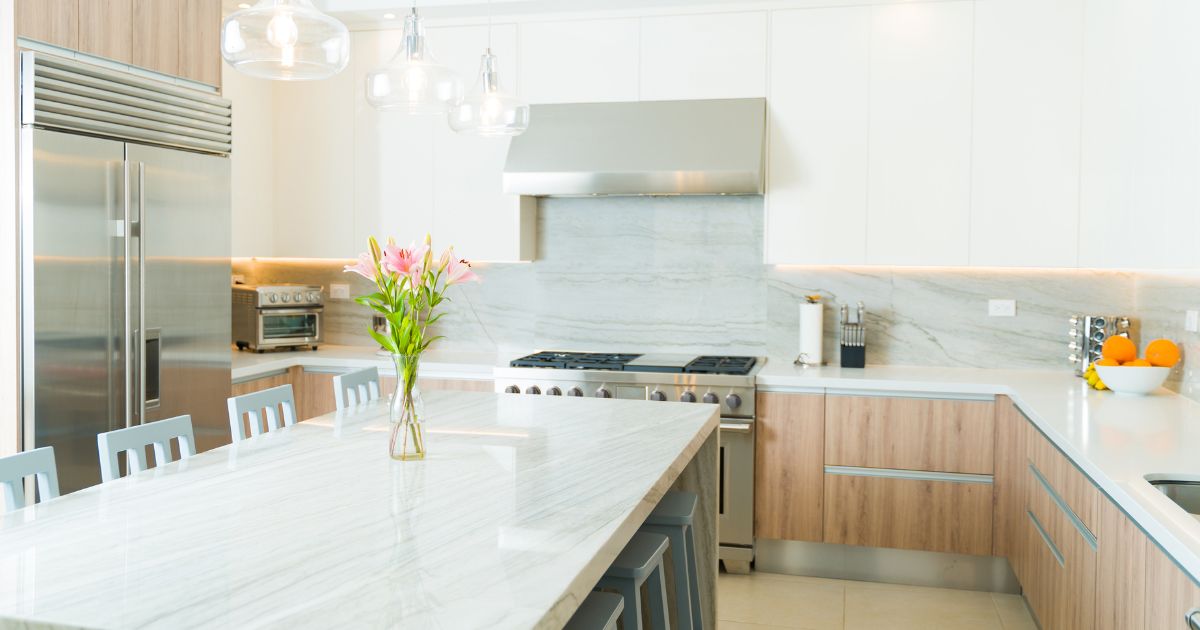 A modern kitchen with a marble island, white cabinetry, stainless steel appliances, and a vase of flowers.