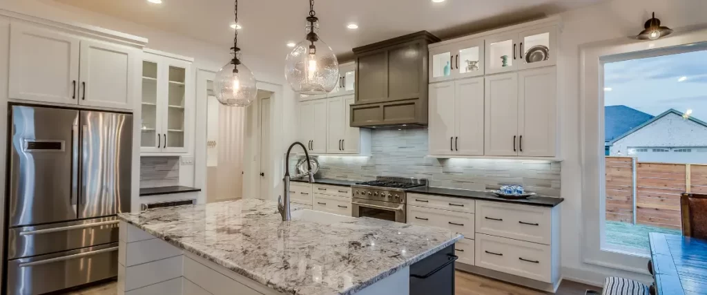 A spacious kitchen with a large granite island, pendant lighting, and a mix of white and dark wood cabinetry.