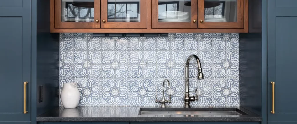 A kitchen sink with a patterned tile backsplash, wooden cabinets, and a black faucet.