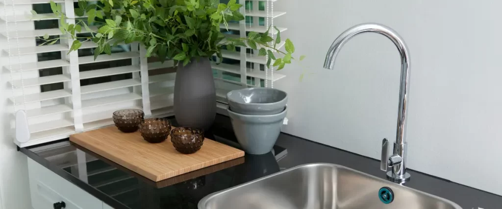 A modern kitchen sink with a chrome faucet, a black countertop, and decorative items, including a plant and small vases.