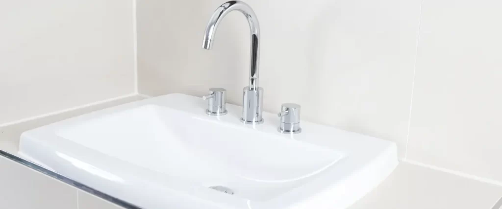 A close-up of a white sink with a chrome faucet and three handles.