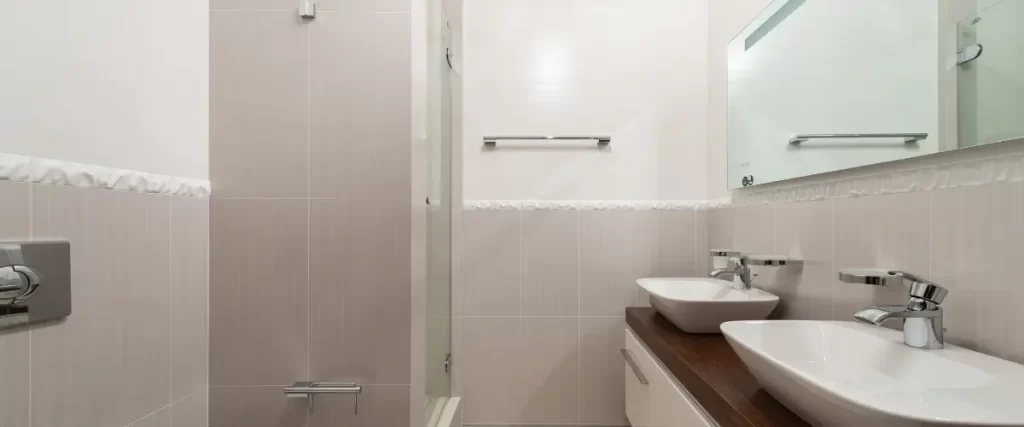 A bathroom with a glass shower door, tiled walls, and a white sink with a wooden countertop.